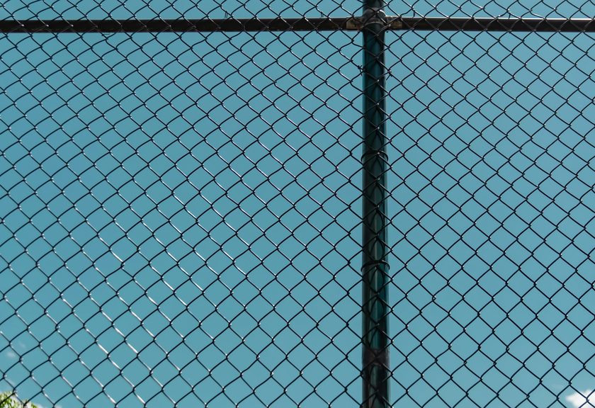 Close view of chain link mesh and a dark post against a blue sky