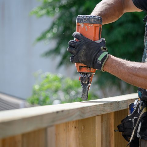 Gloved hand using a nail gun on the top rail of a new wood fence